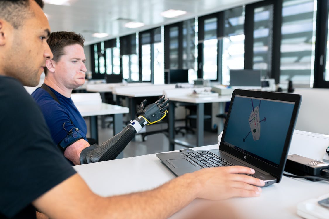 Two people using laptop, one is disabled and is using a engineered arm to function